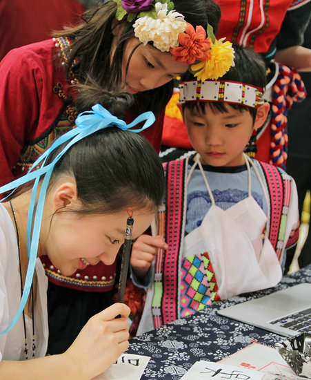 Ruby Yuan, whose heritage is Chinese, uses a calligraphy pen to write phonetically the names of Flora and Leonardo Wu, who attend Westmere Elementary School and came to the Lynnwood school event in traditional Taiwanese costumes. 