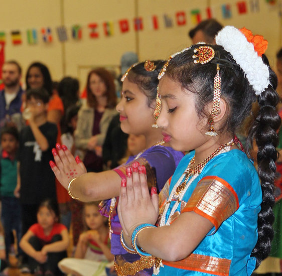 Young girls, the ends of their fingers painted red, hold a still and meditative pose at the start of an Indian dance. 