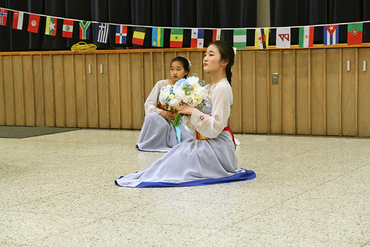 Wearing dresses that layer sheer white over bright blue, two young women strike a pose at the end of a traditional South Korean dance. 