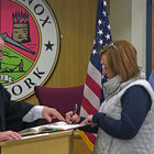 Town Clerk Traci Schanz signs her name after being sworn in New Year’s Day while Supervisor Vasilios Lefkaditis, right, looks on.