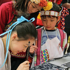 Ruby Yuan, whose heritage is Chinese, uses a calligraphy pen to write phonetically the names of Flora and Leonardo Wu, who attend Westmere Elementary School and came to the Lynnwood school event in traditional Taiwanese costumes. 