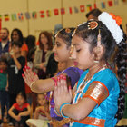Young girls, the ends of their fingers painted red, hold a still and meditative pose at the start of an Indian dance. 
