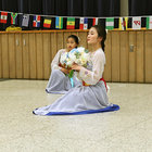 Wearing dresses that layer sheer white over bright blue, two young women strike a pose at the end of a traditional South Korean dance. 