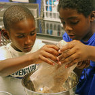 Two boys pour ingredients into a bowl 